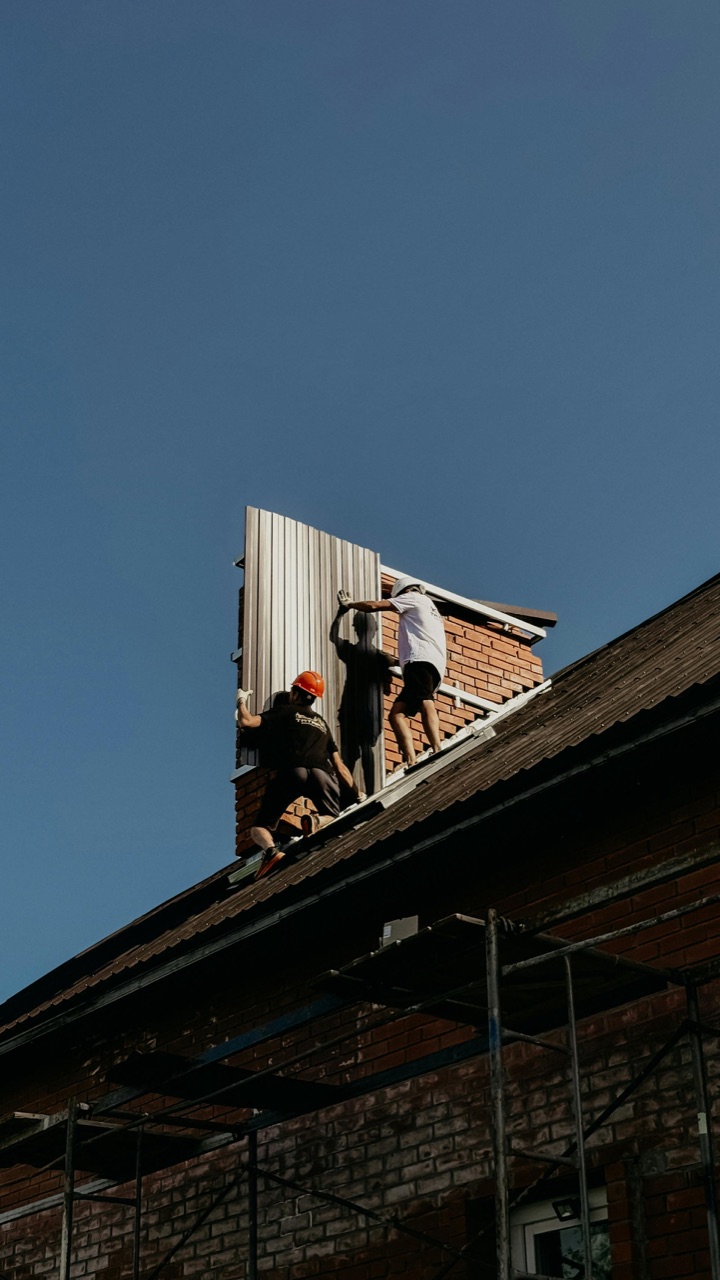 Roofing crew installing metal roof panels on a brick home